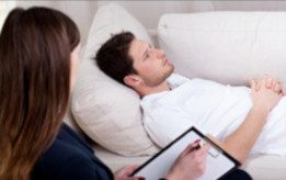 Eine Person liegt entspannt auf einer Couch, während eine andere Notizen macht.