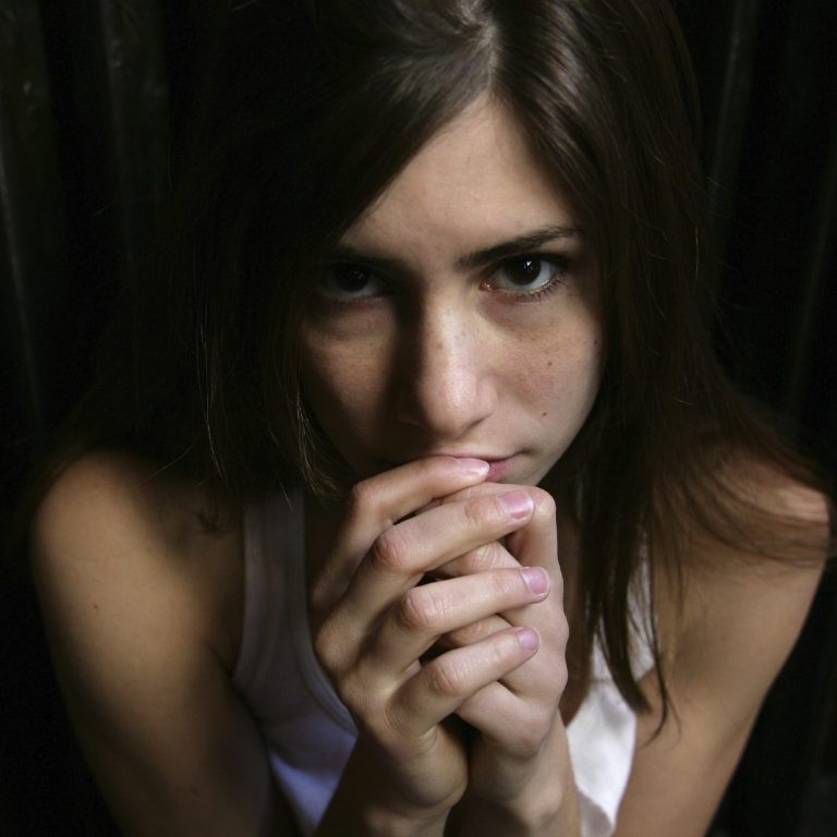 Junge Frau mit dunklen Haaren, die ängstlich die Hände vor dem Gesicht hält.