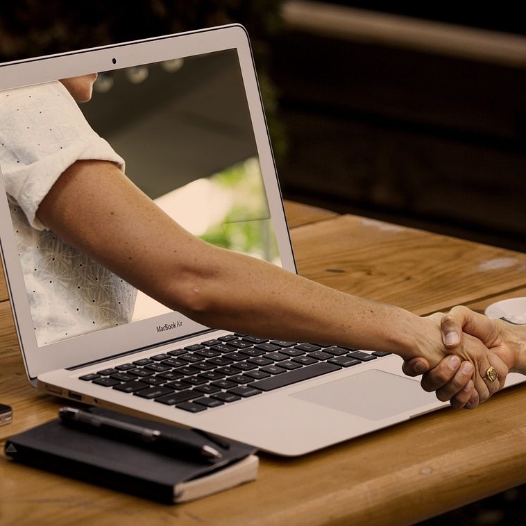 Händeschütteln durch einen Laptop-Bildschirm auf einem Holztisch.